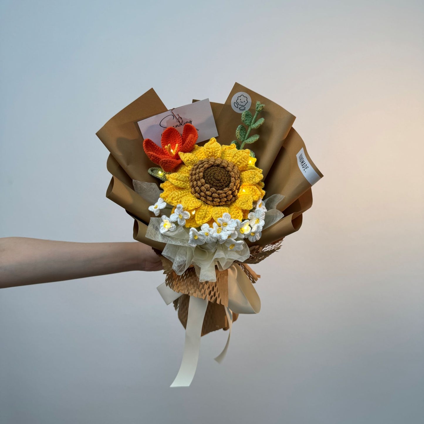 Bouquet with sunflower design held by a hand against a plain background
