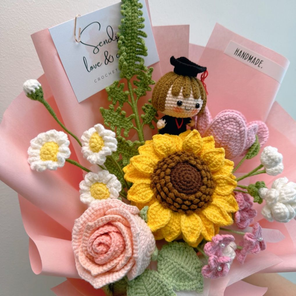 Bouquet of crocheted flowers including a sunflower, roses, and daisies, with a small figurine on top.