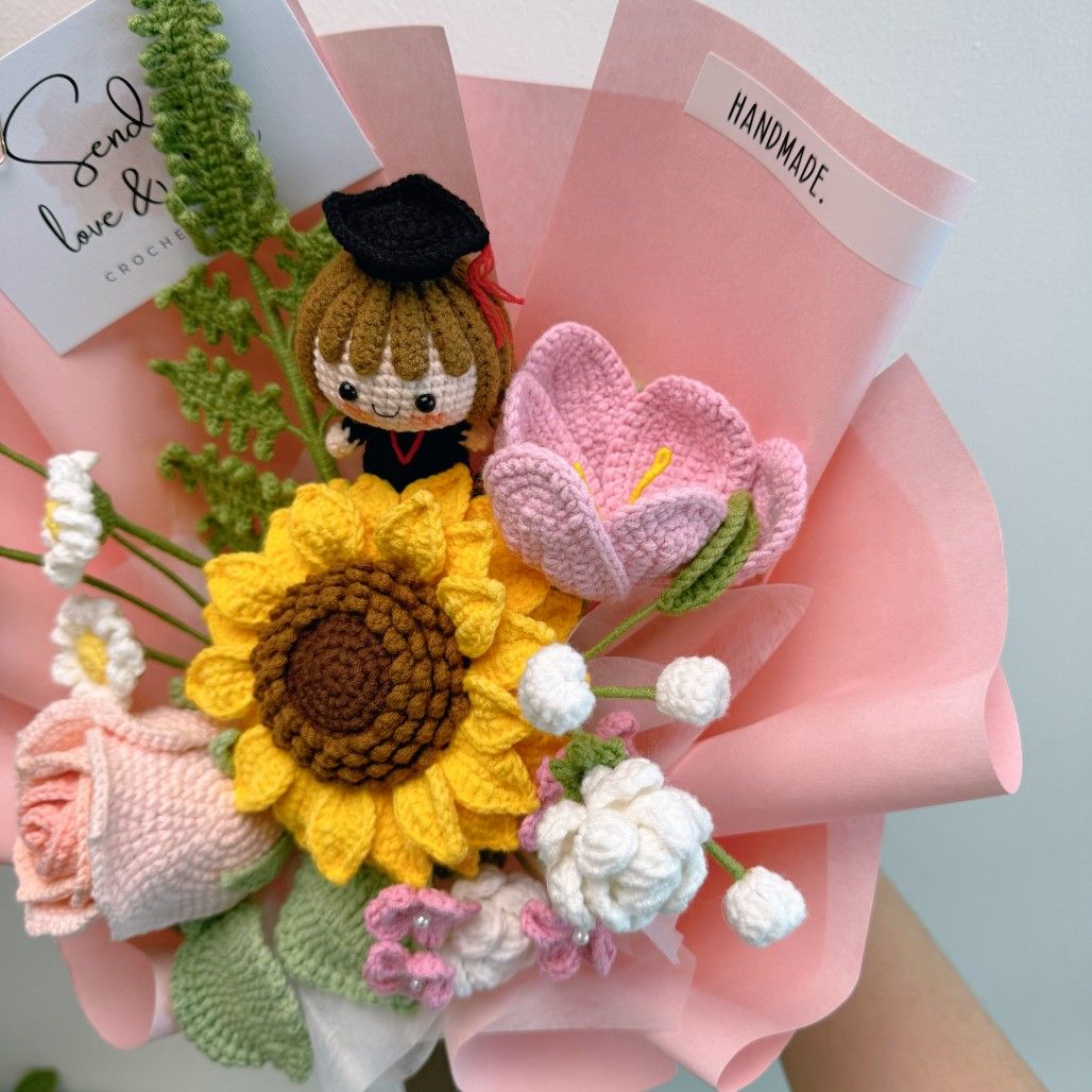 Crocheted flower bouquet with sunflower, pink tulip, and white flowers, featuring a small crocheted doll.