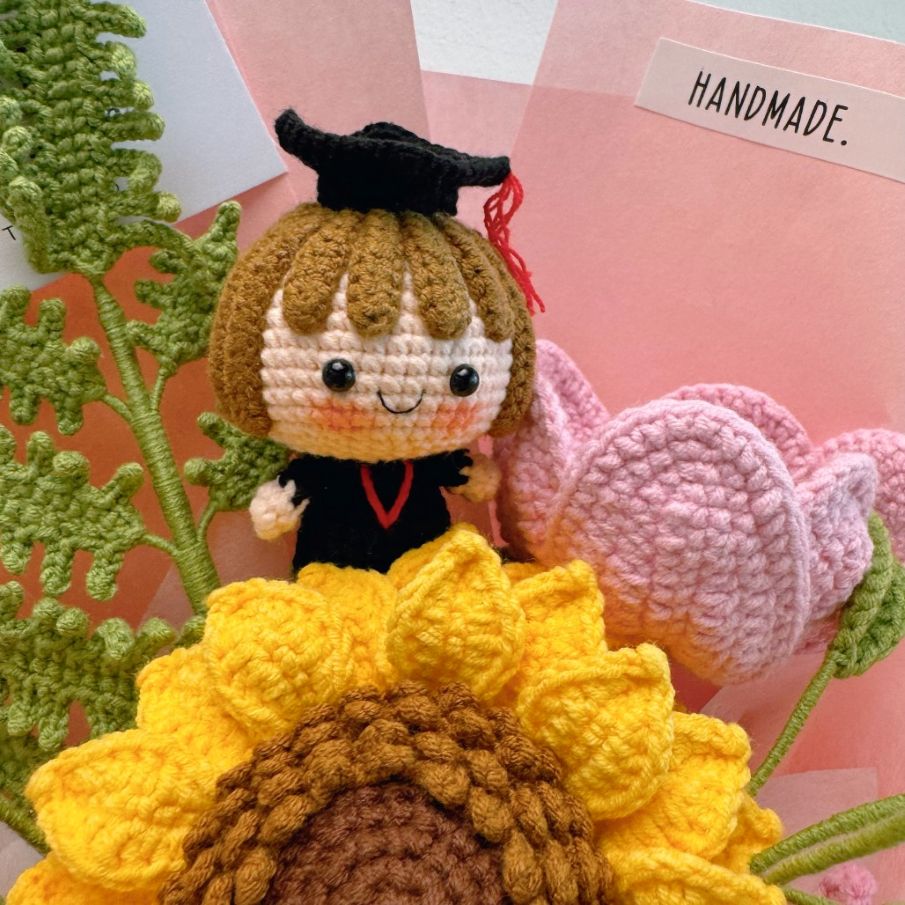 Handmade crochet doll with graduation cap and flowers on a pink background