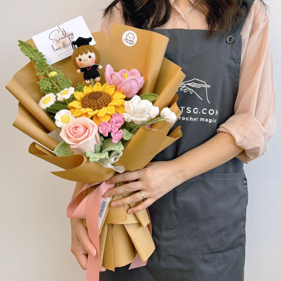 Person holding a bouquet of knitted flowers with a TSG Crochet Magic apron.