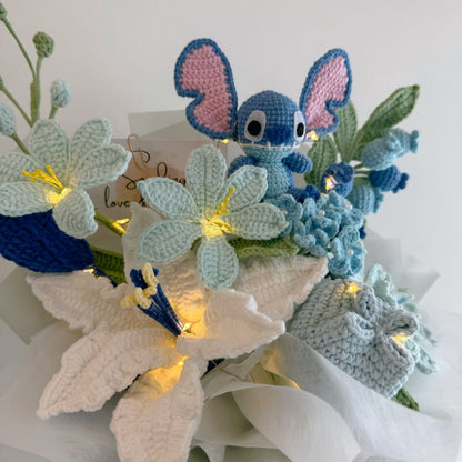 Crocheted flower arrangement with a small blue creature toy on a white background