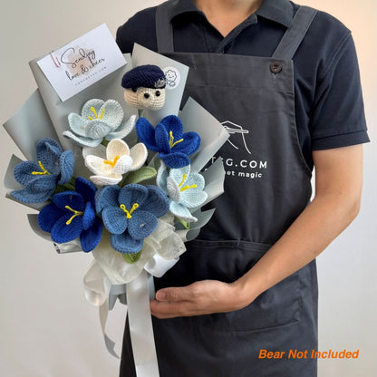 Person holding a bouquet of knitted flowers with a card, wearing an apron with a website address.