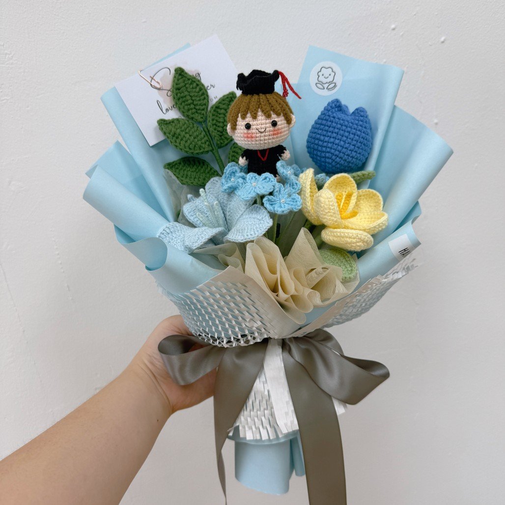 Bouquet of knitted flowers with a small figurine held by a hand against a white background