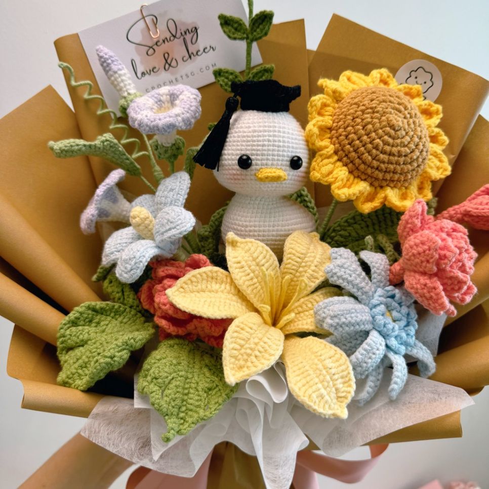 Bouquet of crocheted flowers and a small crocheted character with a yellow sunflower in the center.