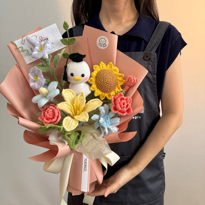 Person holding a bouquet of knitted flowers and a small plush toy against a neutral background