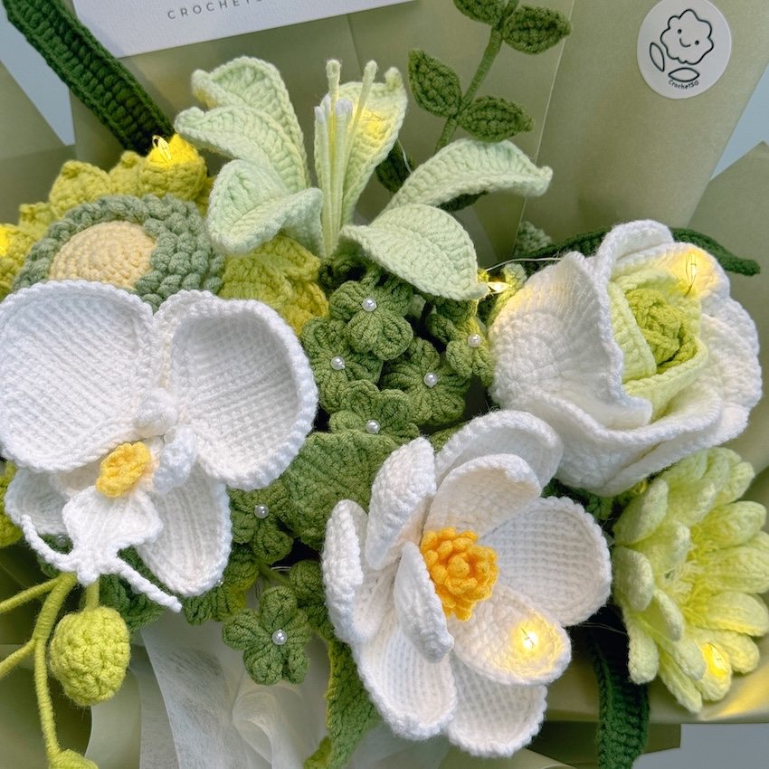 Close-up of a bouquet of crocheted flowers with green leaves and white and yellow centers.