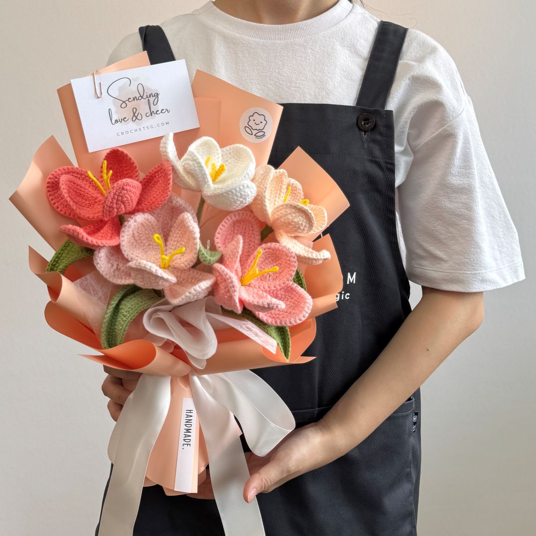 Person holding a bouquet of knitted flowers with a card on a plain background