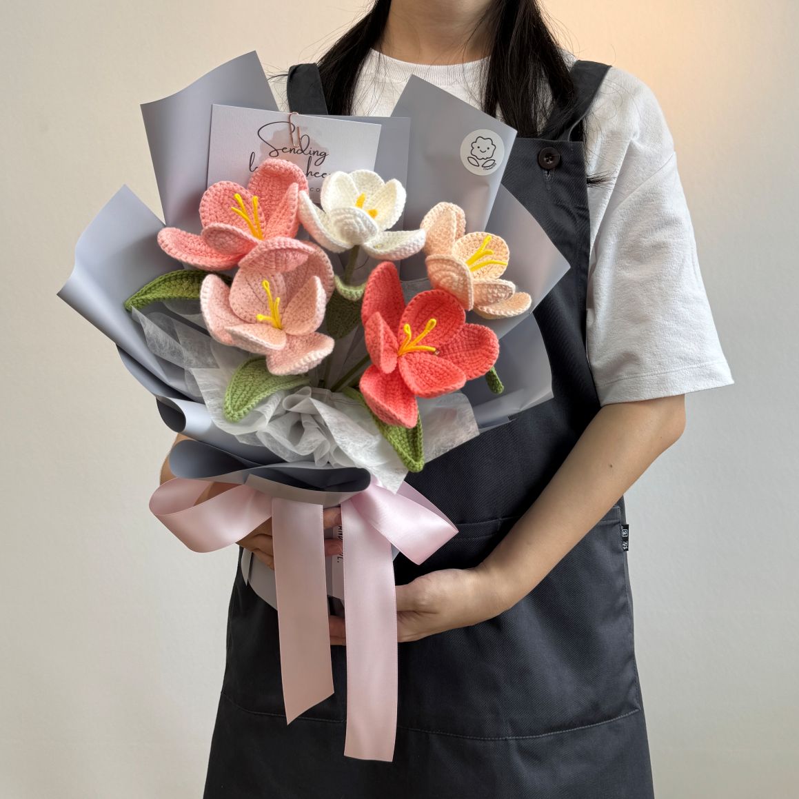 Person holding a bouquet of knitted flowers with gray paper and a pink ribbon.