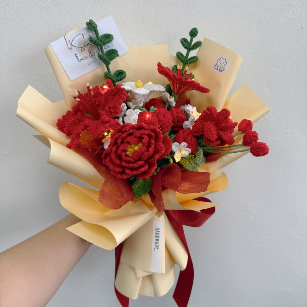 Bouquet of red flowers with yellow ribbons held by a hand against a light gray background