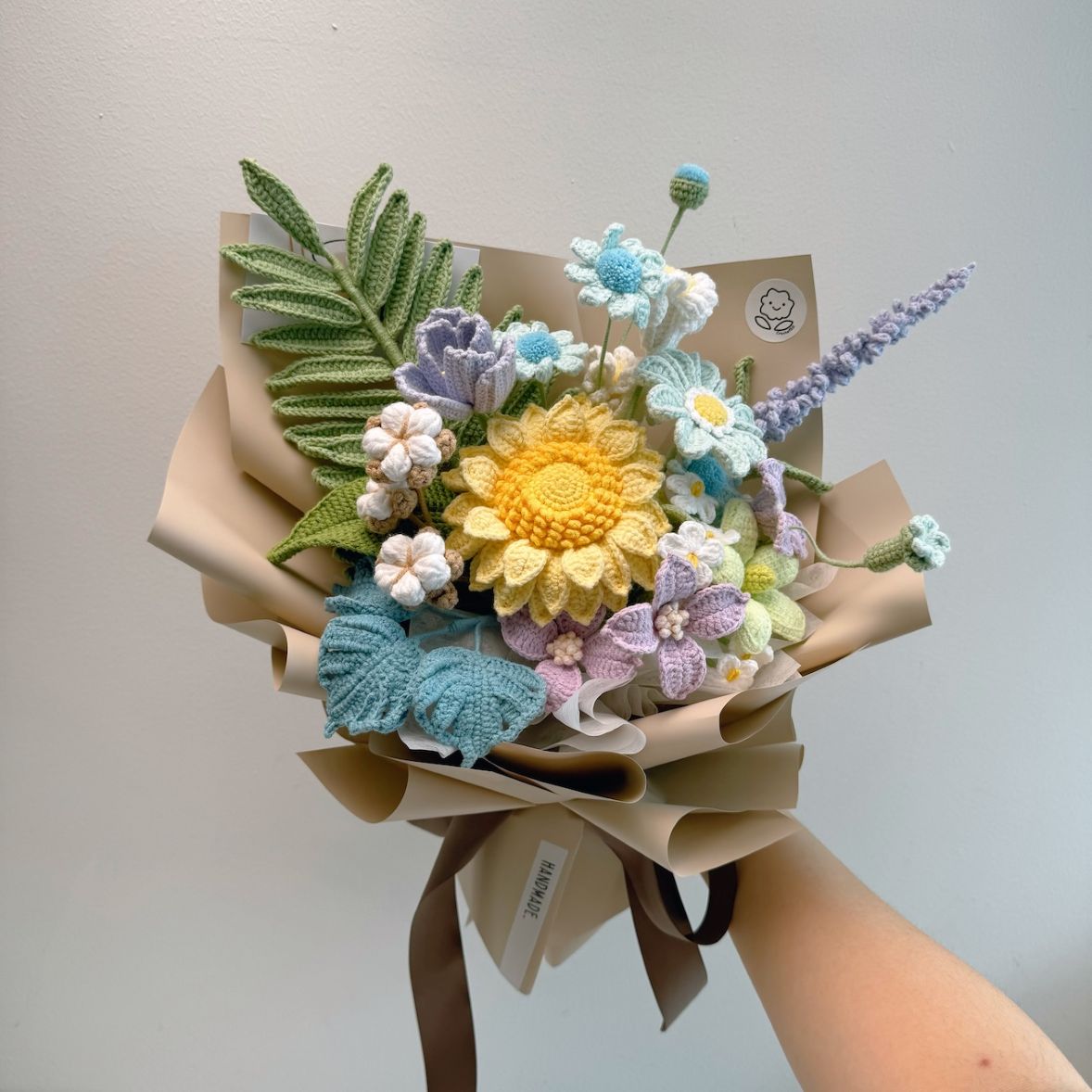 Knitted flower bouquet with a hand holding it against a plain background