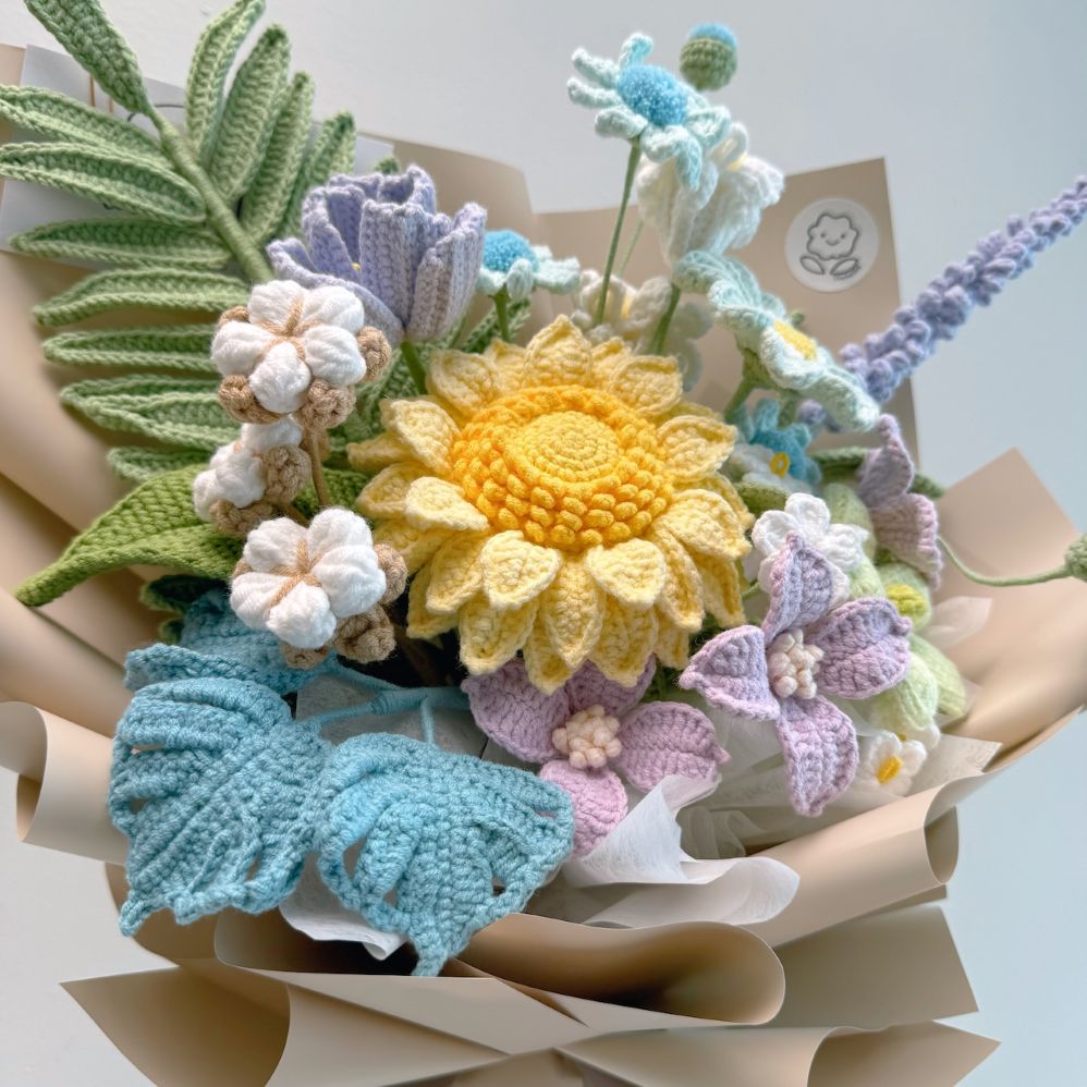 Crocheted flower bouquet with a yellow sunflower and various other flowers on a white background.