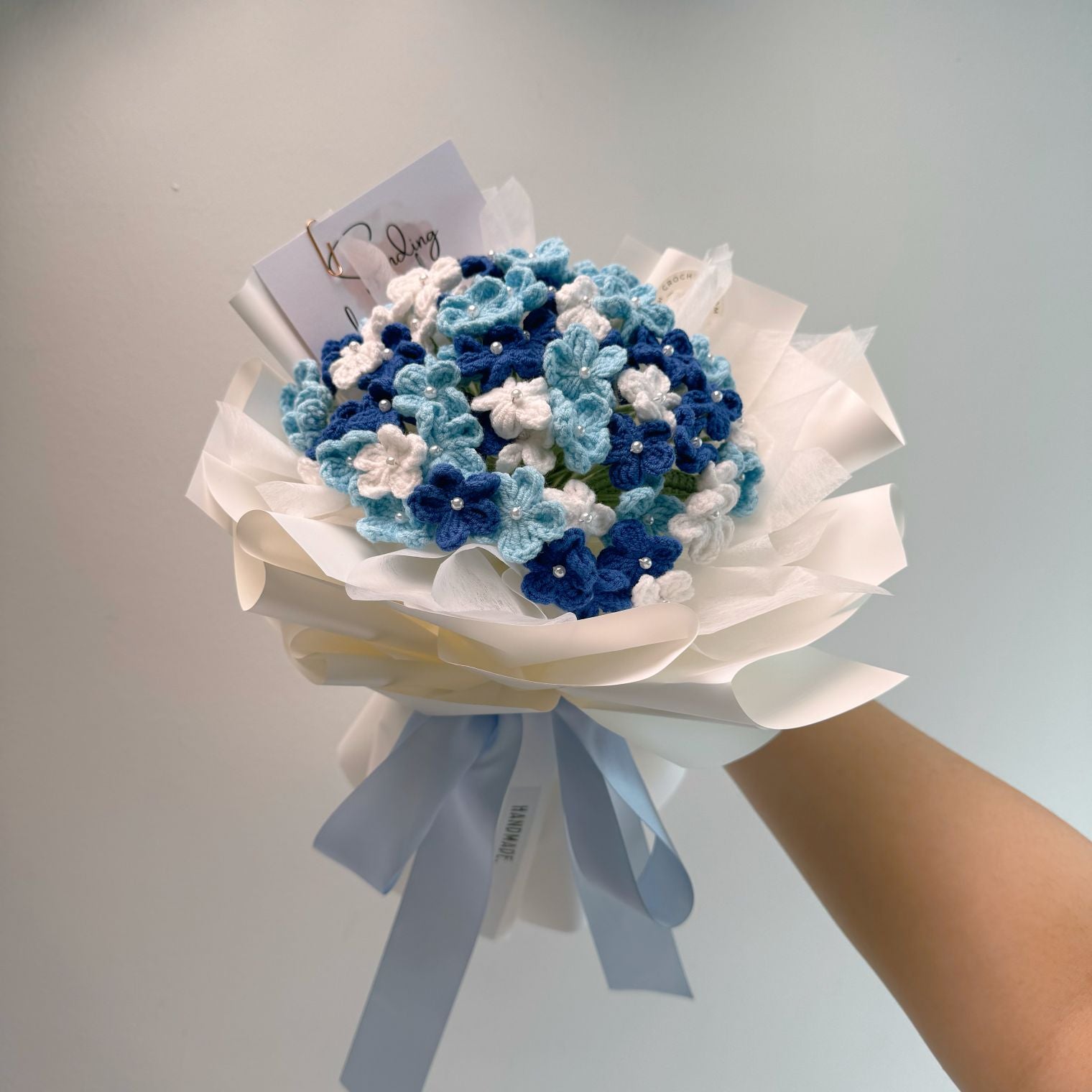 Bouquet of blue and white flowers with a white ribbon on a light gray background