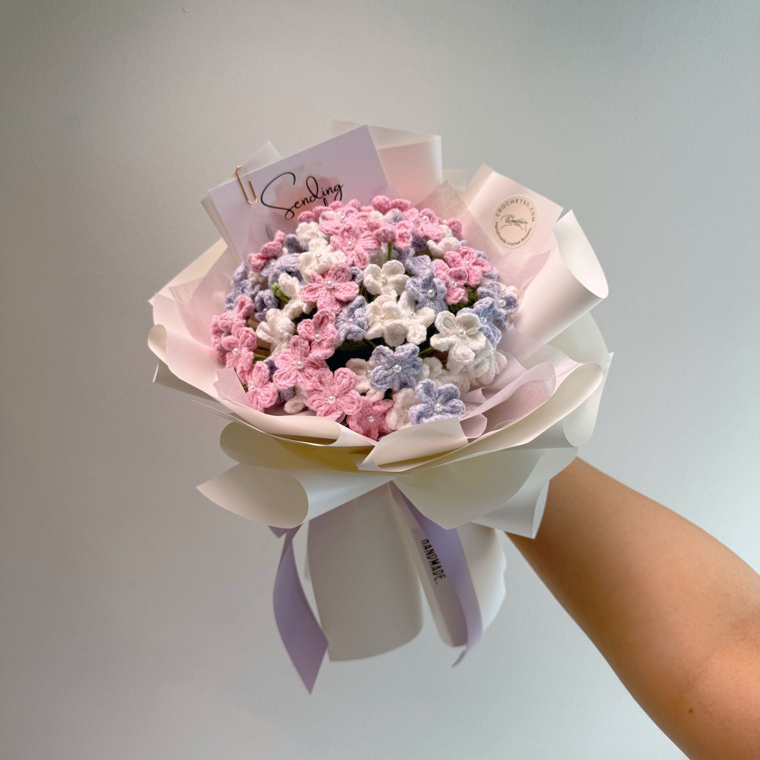 Bouquet of pink, purple, and white flowers held by a person against a light gray background