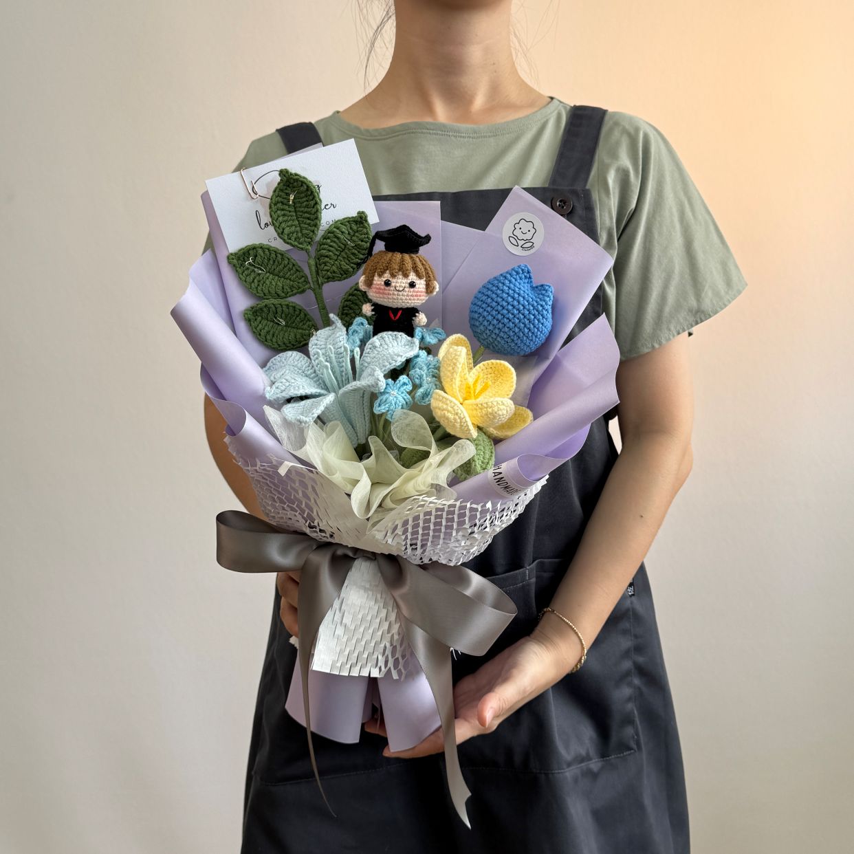 Person holding a bouquet with flowers and a small figurine on a plain background