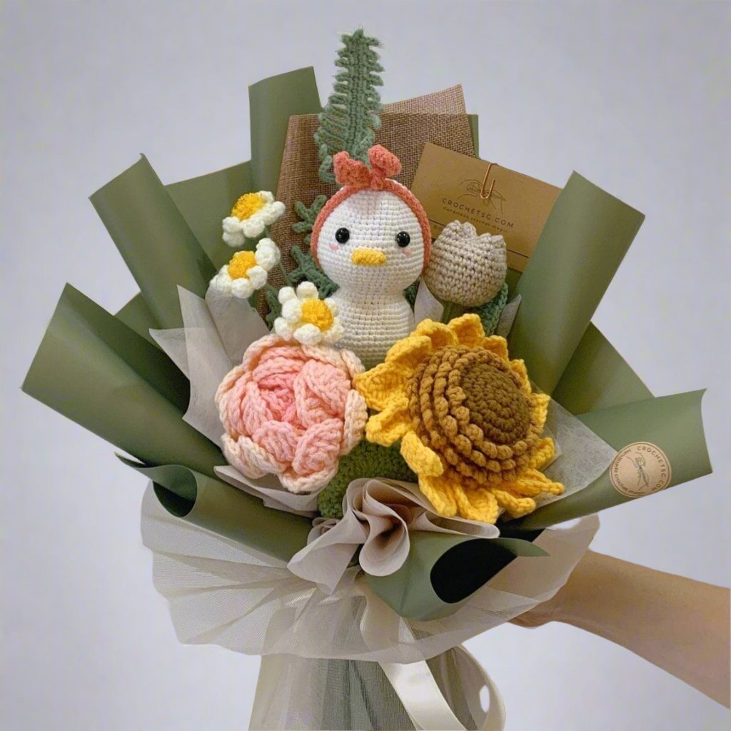 A bouquet of crochet flowers with a sunflower and a crochet duck with pink hairband in the center