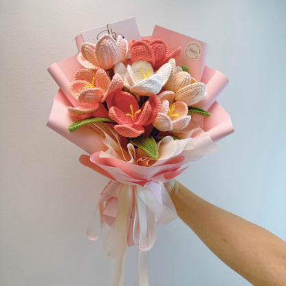 Bouquet of knitted flowers in pink, white, and green held by a hand against a light background